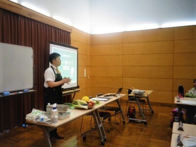 牧野先生が話している様子。机には野菜がたくさん載っています。