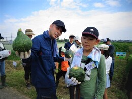 収穫されたひょうたんみたいな変わった形のカボチャを持つ父子。